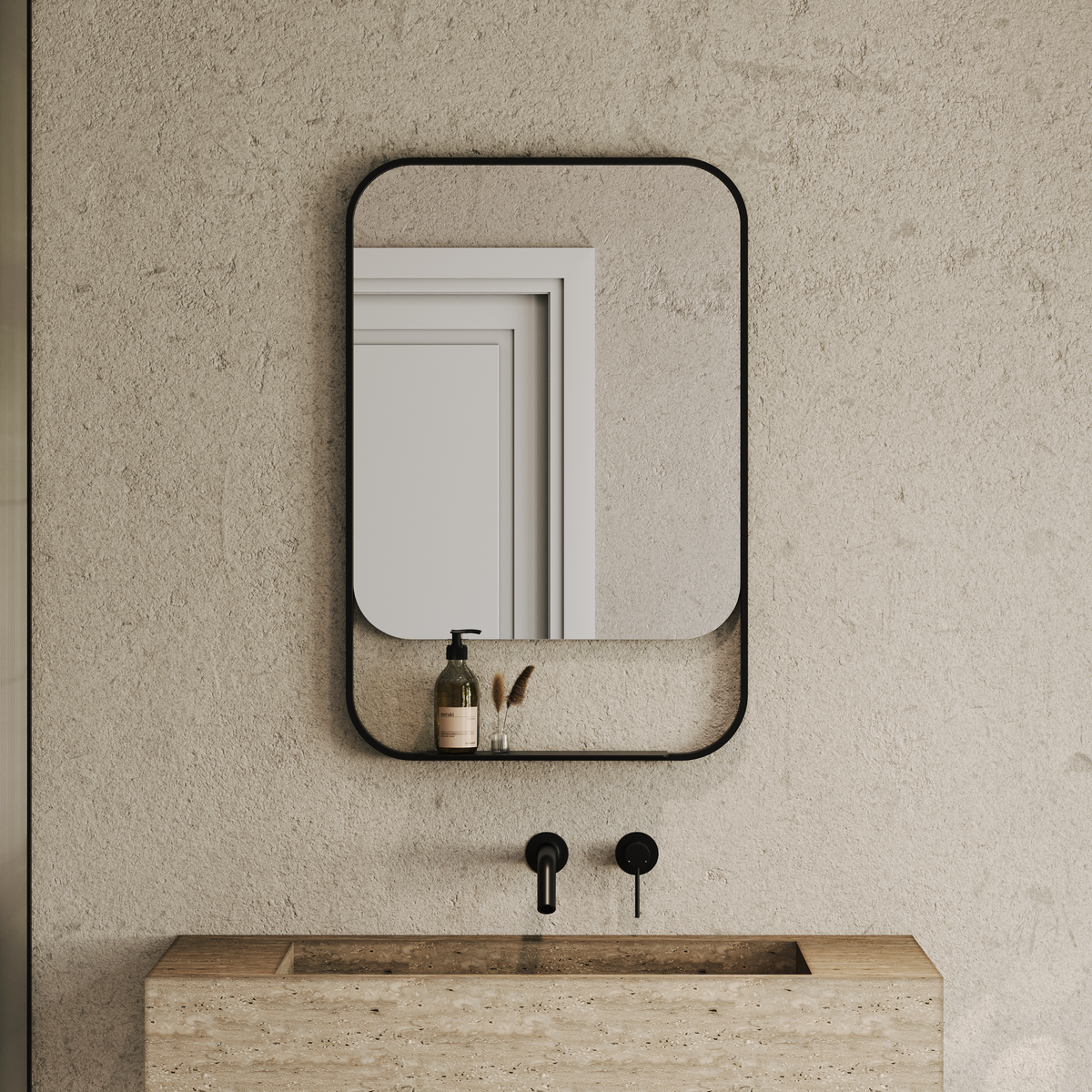 Rounded rectangular mirror with matte black frame and integrated shelf holding a soap dispenser above a stone basin